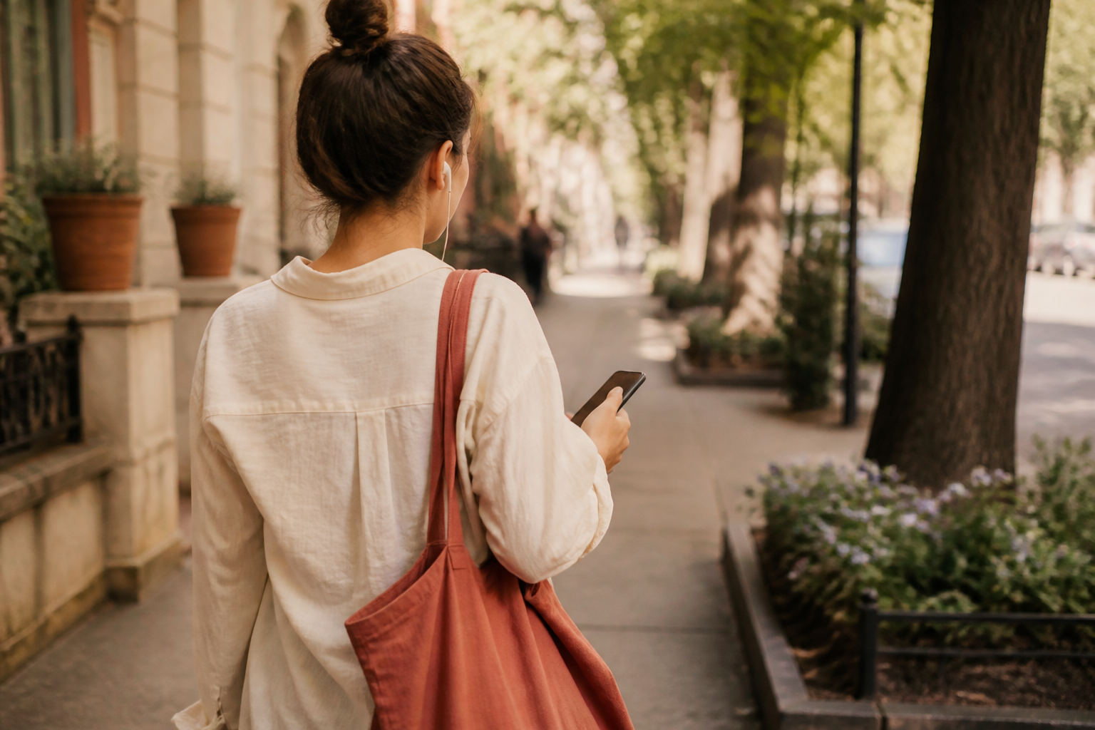 A hand holding a phone during a walk with earbuds in